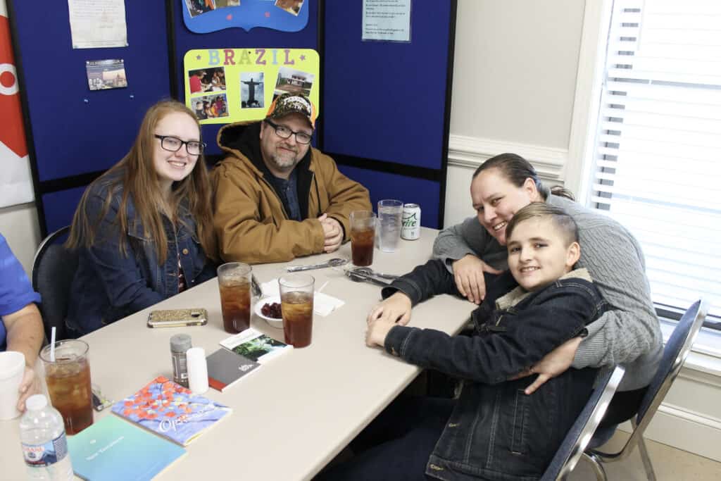 Smiling members of the Harris Family sit together at a table, ready to enjoy a holiday meal made possible by a Second Harvest Partner Agency