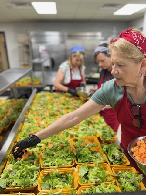 Volunteers prepare fresh salads with lettuce and sliced carrots in a commercial kitchen. The Heimerdinger Foundation, a Second Harvest Partner, provides nutritious meals to cancer patients to support their health and recovery and fight food insecurity