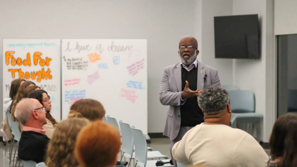 Dr. Holmes, Dean of the College of Liberal Arts and Sciences at Lipscomb University, speaks to an engaged audience about social justice and food insecurity at Second Harvest Food Bank. The event, "Food for Thought," encourages community discussion and advocacy for hunger relief.