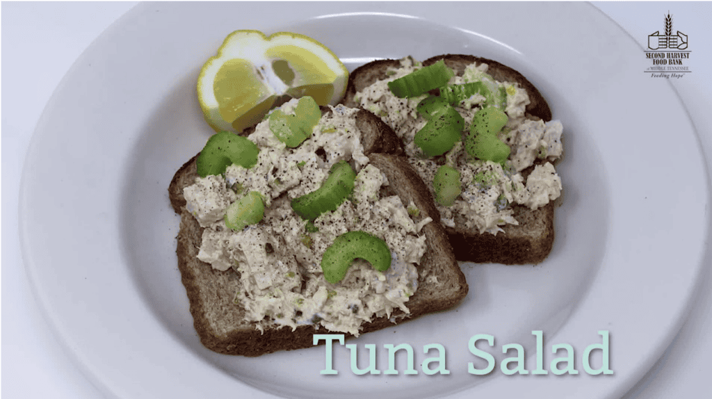 A plate showing healthy food can be simple and affordable. Two slices of whole wheat toast topped with tuna salad, garnished with fresh celery slices and black pepper. Two lemon wedges sit on the plate. The Second Harvest Food Bank of Middle Tennessee logo is in the top right corner, and "Tuna Salad" is written in light blue text at the bottom.