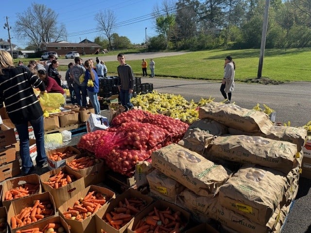 Bags of heart healthy potatoes alongside other fresh vegetables at a Second Harvest mobile pantry with several volunteers. 